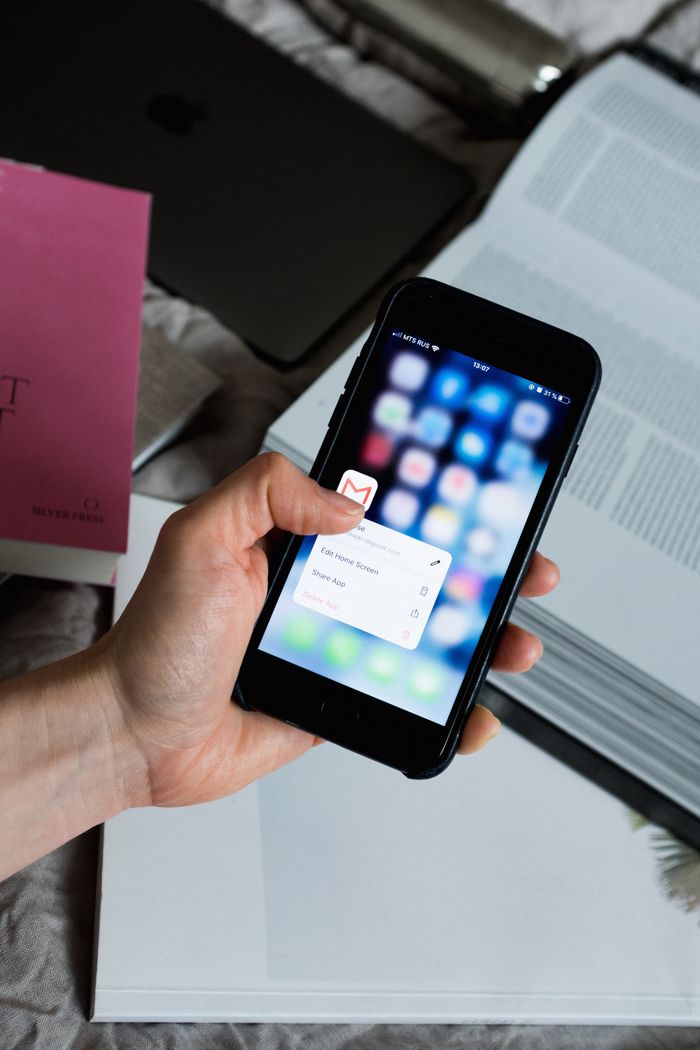 creative-01 Hand holding smartphone with email app open, surrounded by books and laptop.